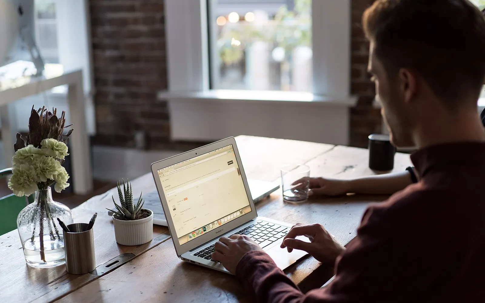 A person typing on a laptop at a wooden desk with a coffee shop window in the background
