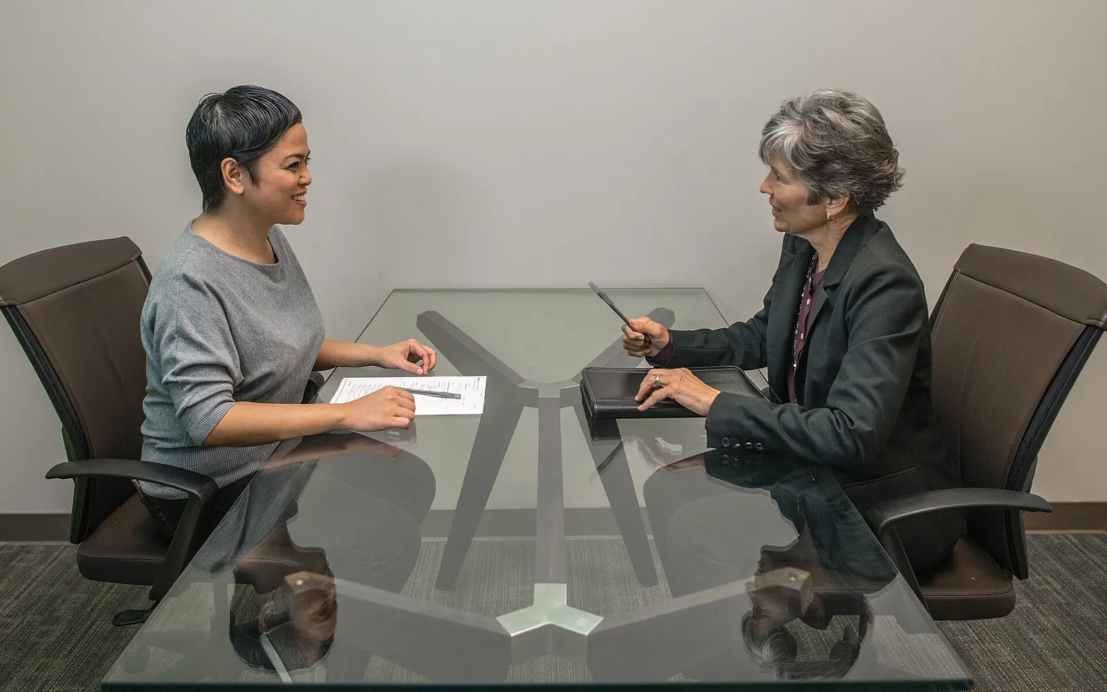 Two people across a glass conference table reviewing a document