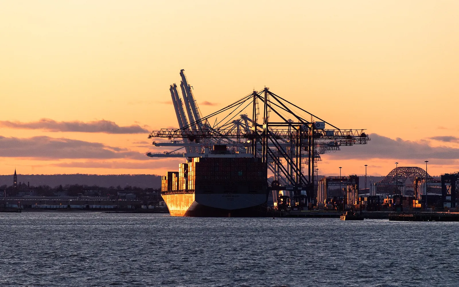 A container ship silhouetted at a port terminal at sunset